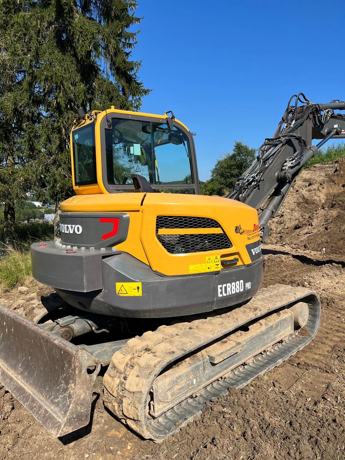 Hans Werner Meyer GmbH - Tiefbauunternehmen - Ein gelb-grauer Volvo ECR88D Pro Kompaktbagger parkt auf einer Baustelle unter strahlend blauem Himmel.
