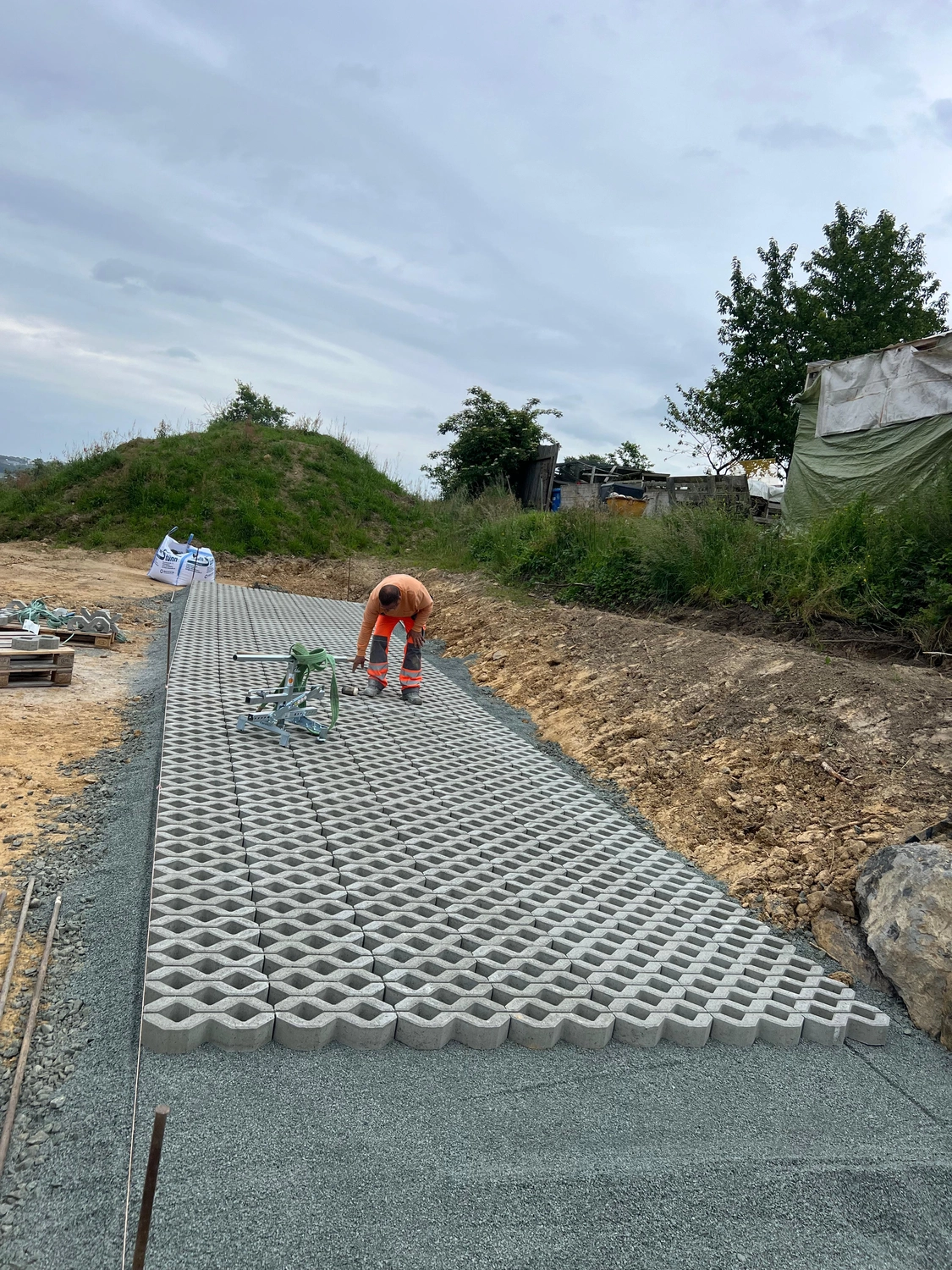 Hans Werner Meyer GmbH - Tiefbauunternehmen - Ein Bauarbeiter verlegt wasserdurchlässige Betonrasenpflastersteine für eine Einfahrt auf einem Kiesbett.